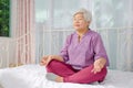 Keep calm and breath. Senior woman meditating in lotus position on bed at home, Healthy morning routine and meditation concept