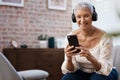 Keep those classics coming. a senior woman using a smartphone and headphones on the sofa at home. Royalty Free Stock Photo