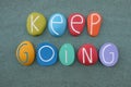 Keep Going text composed with handmade multi colored stone letters over green sand