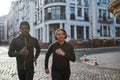 Keep moving. Happy young sporty African couple in headphones jogging, running together through the city street in the Royalty Free Stock Photo