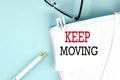 KEEP MOVING text on a sticky on notebook with pen and glasses , blue background