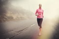 Keep putting one foot in front of the other. A young woman jogging on a country road on a misty morning. Royalty Free Stock Photo
