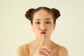 Keep in secret! Portrait of playful positive Asian teen girl with buns hairstyle showing silence gesture over light background