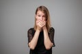 Keep silence. Scared european woman covering mouth with hands while posing to camera on gray studio background. Royalty Free Stock Photo