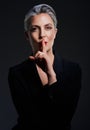 Keep them in suspense. Studio portrait of a beautiful mature woman posing with her finger on her lips against a dark Royalty Free Stock Photo