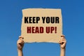 Keep your head up text on box paper held by 2 hands with isolated blue sky background.