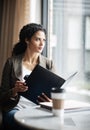 Keeping business moving along. a young businesswoman reading through a business folder in a cafe.