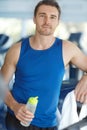 Keeping focussed on his fitness. A happy man leaning on a treadmill at the gym holding a water bottle. Royalty Free Stock Photo