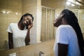 Beautiful young African woman clean face from cosmetics and smiling while standing against a mirror in bathroom Royalty Free Stock Photo