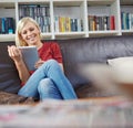 Keeping herself entertained. an attractive young woman sitting on a couch while using a digital tablet.