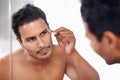 Keeping his eyebrows perfectly symmetrical. A young man plucking his eyebrows while looking in the mirror.
