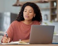 Keeping a note of her upcoming tasks. Shot of a young woman writing notes while working on a laptop at home. Royalty Free Stock Photo