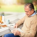 Keeping up with the news of the day. a senior man reading a newspaper with his breakfast outdoors. Royalty Free Stock Photo