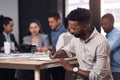 He keeps a note of it all. a young businessman writing in a notebook while sitting in an office with his colleagues in Royalty Free Stock Photo