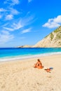 Unidentified young woman sitting on beautiful Petani beach and looking at blue sea, Kefalonia island, Greece