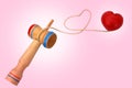 Kendama, a traditional Japanese toy consisting of a sword and a ball connected by a string rolled in heart shape, on pink