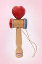 Kendama, a traditional Japanese toy consisting of a sword and a ball connected by a string rolled in heart shape, on pink