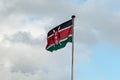 Kenya flag waving in wind against the background of a blue cloudy sky. Royalty Free Stock Photo