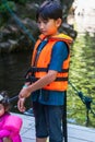 Young boy wearing life jacket is feeding fish at the Kelah Sanctuary in Lubuk Kejor Royalty Free Stock Photo