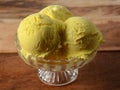 kesar pista ice cream scoops served in a glass bowl over a rustic wooden table, selective focus