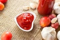 Ketchup in bowl heart shape on sack and wooden background, warm