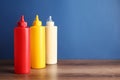 Ketchup, mustard and mayonnaise in squeeze bottles on wooden table against blue background, space for text Royalty Free Stock Photo