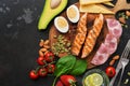 Keto lunch or dinner - grilled salmon, vegetables, boiled egg, water with lime, nuts, ham and cheese on a dark background. Royalty Free Stock Photo