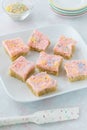 Keto sugar cookie squares topped with pink frosting and coconut sprinkles on a plate ready for serving.