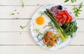 Fried egg, crisp loaves with salmon, green asparagus, fresh tomatoes and red onions on white plate Royalty Free Stock Photo