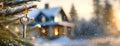 Key hangs on a snowy pine branch with a cozy house in the blurred background. Real estate, moving home or renting