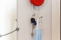 Key holder with Red Button on gray wall near the mirror. Key holder with medical mask and keys hanging on the wall Royalty Free Stock Photo