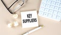 KEY SUPPLIERS text on sticky with pen ,calculator and glasses on a beige background
