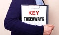 KEY TAKEAWAYS is written on a white sheet held by a man standing sideways Royalty Free Stock Photo