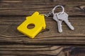 Key with yellow shaped house keychain on chain on wood texture background. Royalty Free Stock Photo