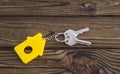 Key with yellow shaped house keychain on chain on wood texture background.