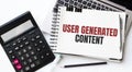 Keyboard of laptop, calcualtor, pencil and notepad with text USER GENERATED CONTENT on the white background