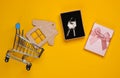 Keys in a gift box with a bow, house figure, shopping trolley on a yellow background. Top view