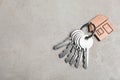 Keys with trinket in shape of house on stone background, top view and space for text. Real estate agent services