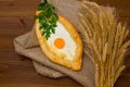 Khachapuri with egg and wheat ears on sacking, dark wooden table Royalty Free Stock Photo