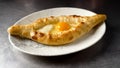 Khachapuri on a plate on the table close-up. A plate with delicious Adjarian khachapuri on a dark table background