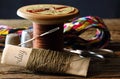 KHAKI COLORED THREAD AROUND A PIECE OF PAPER WITH A WOODEN COTTON REEL WITH TRHEAD, SCISSORS, THIMBLES, NEEDLE AND COLORFUL THREA