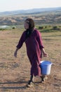 Asian woman from a rural area walking to the stable carrying a blue plastic bucket at milking time. Mongolia