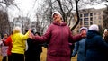 A happy older woman enthusiastically dances in the city park. Entertainment of old people
