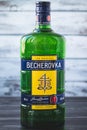 Kharkiv, Ukraine, November 15, 2019: A full glass green bottle of becherovka on gray wooden background. Strong drink - czech