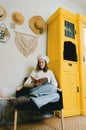 Kharkiv, Ukraine. 01.22.2022. Young woman in beret sits in an armchair in cozy home, in room with music record in hands. Vintage