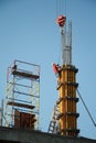 A construction worker controls the crane movement when assembling building blocks against a blue sky