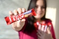 KHARKOV, UKRAINE - OCTOBER 21, 2019: A young caucasian brunette girl shows kit kat chocolate bar in red wrapping in light room.