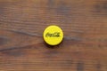 Single yellow bottle lid with Coca Cola logo on wooden background
