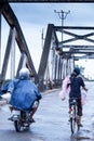 Khmer people riding motorcycles and bicycle across over the old French Bridge on rainy morning, Kampot, Cambodia Royalty Free Stock Photo