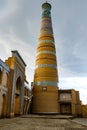 Khodja minaret and mosque madrasah in the historical center of Khiva with dark rain clouds, Uzbekistan